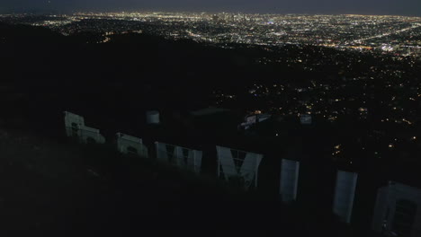 AERIAL:-Spectacular-Flight-Close-over-Hollywood-Sign-Letter-at-Night-with-Los-Angeles-Cityscape-Lights