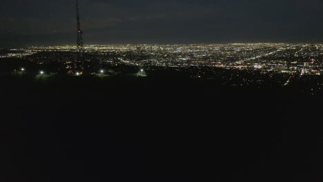 AERIAL:-Spectacular-Flight-over-Mount-Lee-and-Hollywood-Sign-at-Night-with-Los-Angeles-Cityscape-Lights