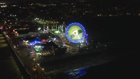 AERIAL:-Breathtaking-view-on-Santa-Monica-Pier-at-night-with-Ferris-Wheel-and-colorful-lights,