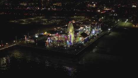 AERIAL:-Breathtaking-view-on-Santa-Monica-Pier-at-night-with-Ferris-Wheel-and-colorful-lights,