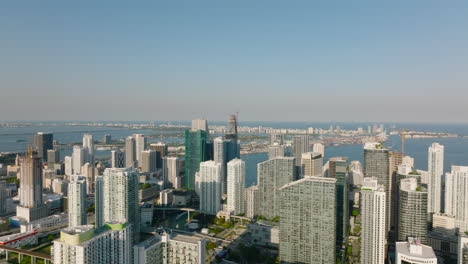 Aerial-ascending-footage-of-modern-residential-complex-of-high-rise-apartment-buildings,-Water-surface-in-sea-bay-in-background.-Miami,-USA