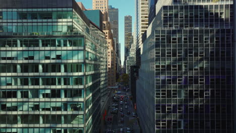 Fly-above-long-straight-street-leading-through-midtown.-Various-office-or-commercial-buildings-with-many-windows.-Manhattan,-New-York-City,-USA