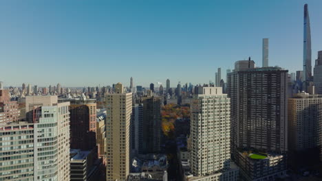 Rising-footage-of-tall-buildings,-revealing-view-of-various-buildings-in-city-and-autumn-foliage-in-park.-Manhattan,-New-York-City,-USA