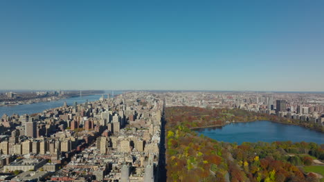 Sunny-autumn-day-in-city.-Forwards-fly-above-colourful-central-park-and-town-development-around.-Manhattan,-New-York-City,-USA