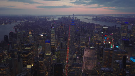 Panoramic-aerial-view-of-large-city-surrounded-by-water-in-twilight-time.-High-rise-buildings-and-traffic-on-avenues.-Manhattan,-New-York-City,-USA