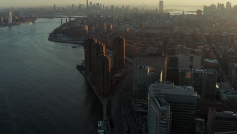 Aerial-panoramic-shot-of-cityscape-against-setting-sun.-Busy-road-on-waterfront.-Manhattan,-New-York-City,-USA