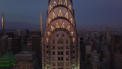Pull-back-shot-of-illuminated-decorative-crown-on-top-of-high-rise-Chrysler-Building.-Skyscrapers-at-dusk.-Manhattan,-New-York-City,-USA