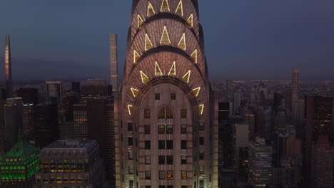 Tiro-Hacia-Atrás-De-La-Corona-Decorativa-Iluminada-En-La-Parte-Superior-Del-Edificio-Chrysler-De-Gran-Altura.-Rascacielos-Al-Anochecer.-Manhattan,-Ciudad-De-Nueva-York,-Estados-Unidos