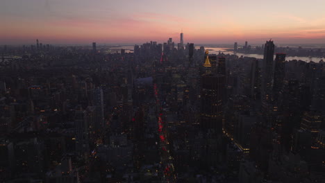 Aerial-view-of-city-development-at-dusk.-Tilt-up-reveal-cityscape-against-colourful-twilight-sky.-Manhattan,-New-York-City,-USA