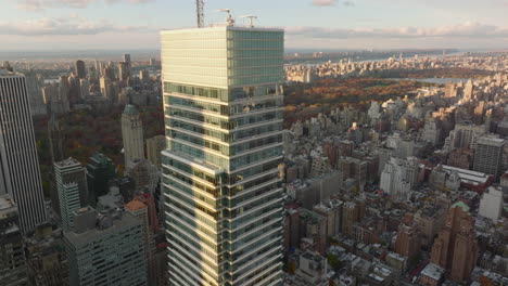 Aerial-view-of-upper-section-of-Bloomberg-Tower-above-other-town-development.-Autumn-colour-trees-in-Central-Park-in-background.-Manhattan,-New-York-City,-USA