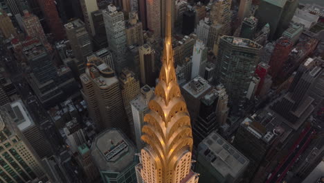 Fly-over-decorative-crown-and-tall-spire-on-top-of-Chrysler-Building-lit-by-golden-sunset-light.-Manhattan,-New-York-City,-USA