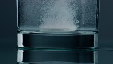 White-tablet-dissolving-water-in-transparent-cup-closeup.-Fizzy-pill-bubbling