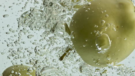 Closeup-apples-splashing-water-in-light-background.-Tasty-green-fruits-falling