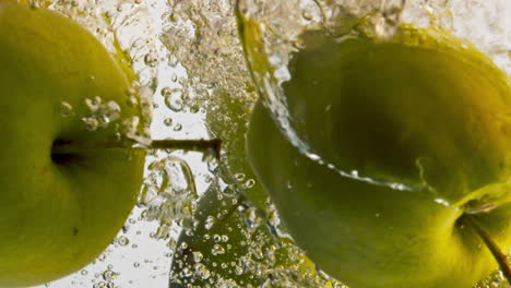 Manzanas-Enteras-Cayendo-Agua-De-Cerca.-Las-Frutas-Verdes-Y-Amargas-Fluyen-En-Un-Fondo-Claro.