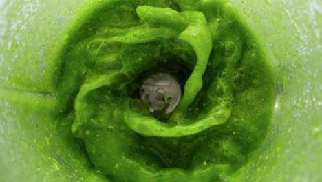 Adding-fresh-greens-smoothie-swirling-in-blender-closeup.-Organic-food-in-mixer