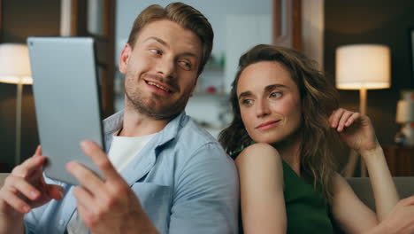 Laughing-man-showing-tab-wife-indoors-zoom-on.-Closeup-two-people-using-gadgets