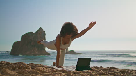 Woman-watching-yoga-online-lesson-using-tablet-morning-sand-beach-vertical-video