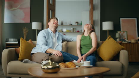 Excited-spouses-laughing-sofa-interior.-Happy-smiling-family-having-fun-at-home