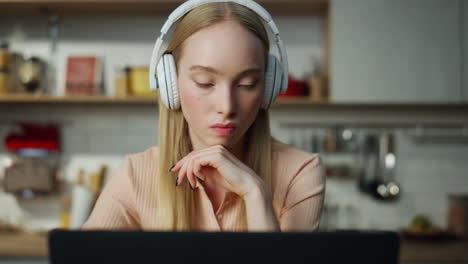 Girl-looking-laptop-screen-searching-in-internet-listening-music-by-headphones