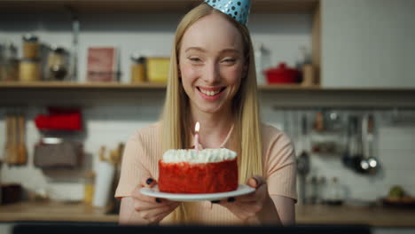 Girl-holding-cake-smiling-on-laptop-web-camera-closeup.-Girl-blowing-on-candle.