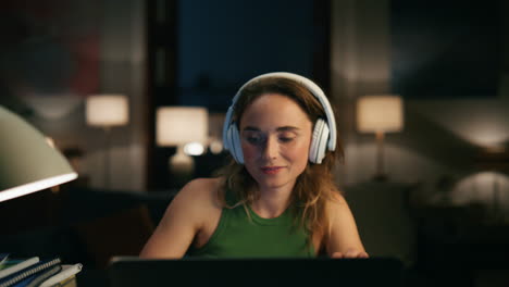 Young-specialist-working-laptop-night-closeup.-Headphones-girl-listening-podcast