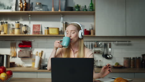 Chica-Escuchando-Música-Con-Auriculares-Sentada-En-La-Cocina-Con-Una-Computadora-Portátil.-Mujer-Relajante.