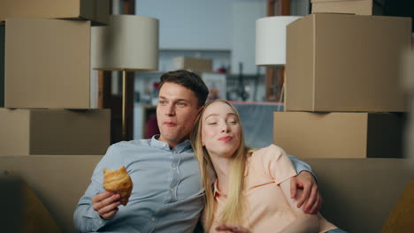 Happy-family-rent-new-house-eating-croissant-on-couch-living-room-close-up.