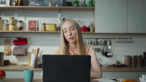 Administrador-En-Línea-Que-Consulta-La-Computadora-Portátil-Con-Cámara-Web-De-Forma-Remota-En-La-Cocina.-Chica-Trabajando-En-Casa.