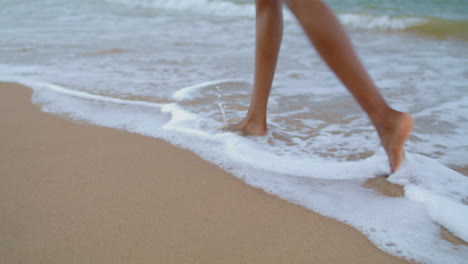 Closeup-legs-walking-ocean-beach.-Slim-woman-feet-going-splashing-waves-alone.