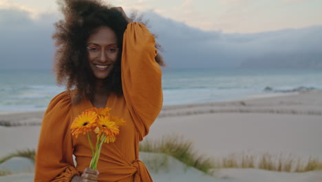 Porträt-Einer-Frau,-Die-Vor-Einem-Düsteren-Himmel-Am-Strand-Blumen-Schnuppert.-Lächelndes,-Lockiges-Mädchen