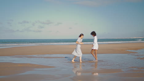Happy-girlfriends-hug-beach-in-sunlight.-Vertical-lesbian-couple-laughing-ocean