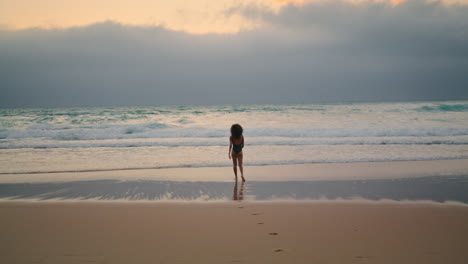 Exotic-model-posing-waves-cloudy-evening.-Woman-walking-on-wet-sand-near-ocean.