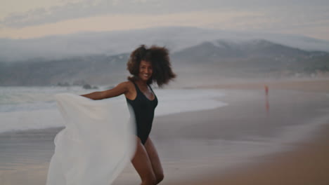 Girl-spinning-beach-shawl-summer-twilight.-Woman-waving-pareo-smiling-at-camera.