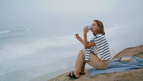 Girl-drink-cliff-coffee-on-summer-weekend-vertical.-Serene-tourist-enjoy-ocean