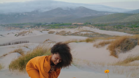 Smiling-woman-taking-flowers-at-gloomy-desert.-Girl-dancing-sniffing-blossom.