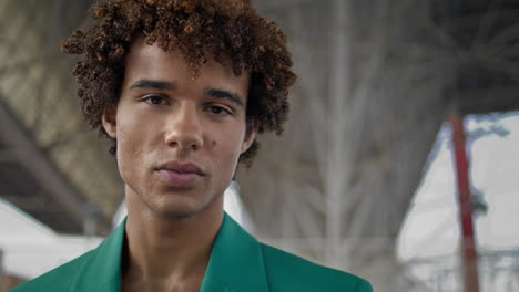 Elegant-guy-smiling-camera-at-street-closeup.-Curly-hair-model-posing-vertically