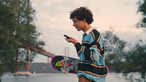 Smiling-student-walking-mobile-at-coast-closeup.-Skater-listening-voice-message