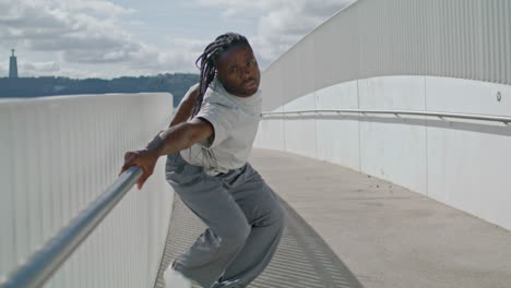 Dreadlocks-man-dancing-bridge-closeup.-Sensual-guy-touching-fence-looking-camera