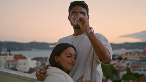 Tender-couple-enjoying-honeymoon.-Brunette-man-drinking-white-wine-at-sunset