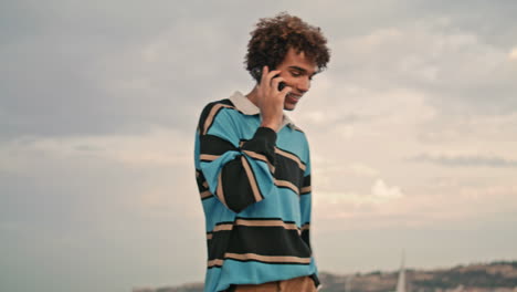 Smiling-student-walking-mobile-river-view-place.-Happy-young-man-touching-hair