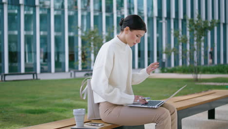 Woman-working-laptop-sitting-at-bench-outdoors.-Lady-work-remotely-vertically