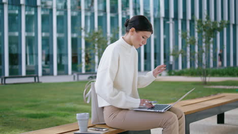 Mujer-Trabajando-Con-Computadora-Portátil-Sentada-En-Un-Banco-Al-Aire-Libre.-Señora-Trabaja-Remotamente-Verticalmente