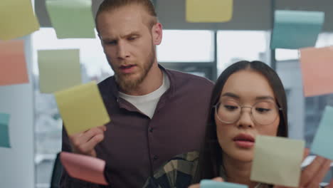 Involved-girl-attaching-stickers-at-transparent-wall-close-up.-Man-reading-notes