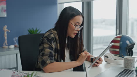 Una-Señora-Pensativa-Escribiendo-Una-Tableta-En-El-Primer-Plano-Del-Lugar-De-Trabajo.-Mujer-Mirando-La-Pantalla-De-La-Plataforma