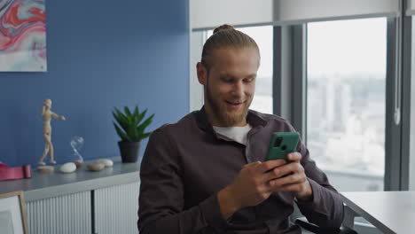 Relaxed-guy-messaging-smartphone-at-office-close-up.-Freelancer-resting-armchair