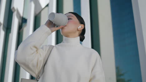 Girl-drinking-coffee-takeaway-standing-in-front-city-building-closeup-vertically