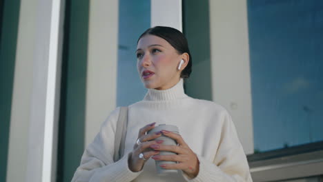 Woman-talking-wireless-earphones-in-front-urban-building-close-up-vertical-view.