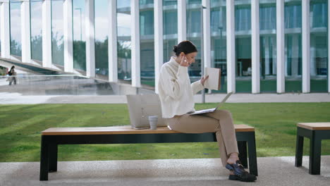 Businesswoman-starting-online-meeting-putting-on-earbuds-outdoor-vertical-view