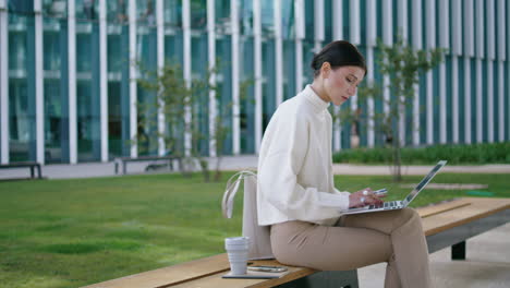 Business-woman-working-remotely-on-laptop-sitting-bench-vertically-typing-report