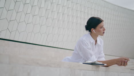 Woman-enjoy-work-break-outdoors-leaning-fence-in-earbuds.-Girl-listening-music.